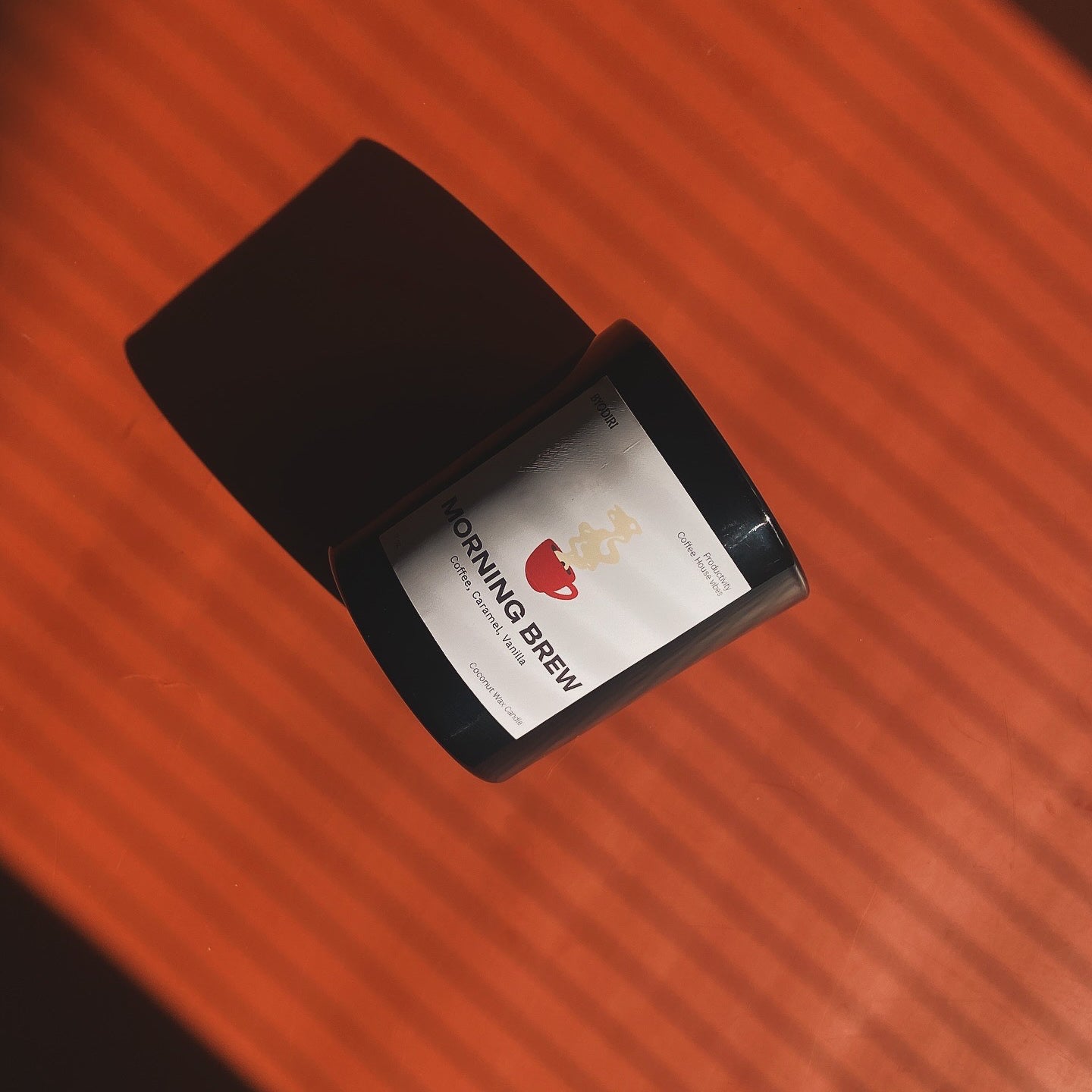 Black candle jar displaying 'Morning Brew' on a red brown surface