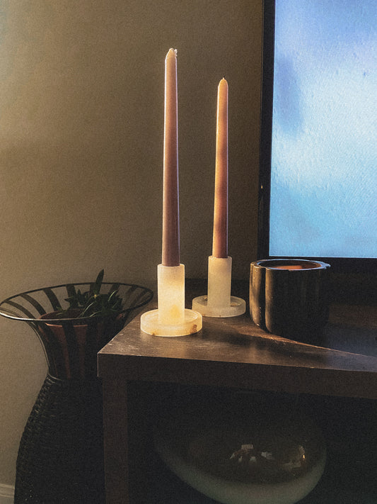 Clear taper candle holders sitting on a a tv stand in a dim room with the sunlight peaking in