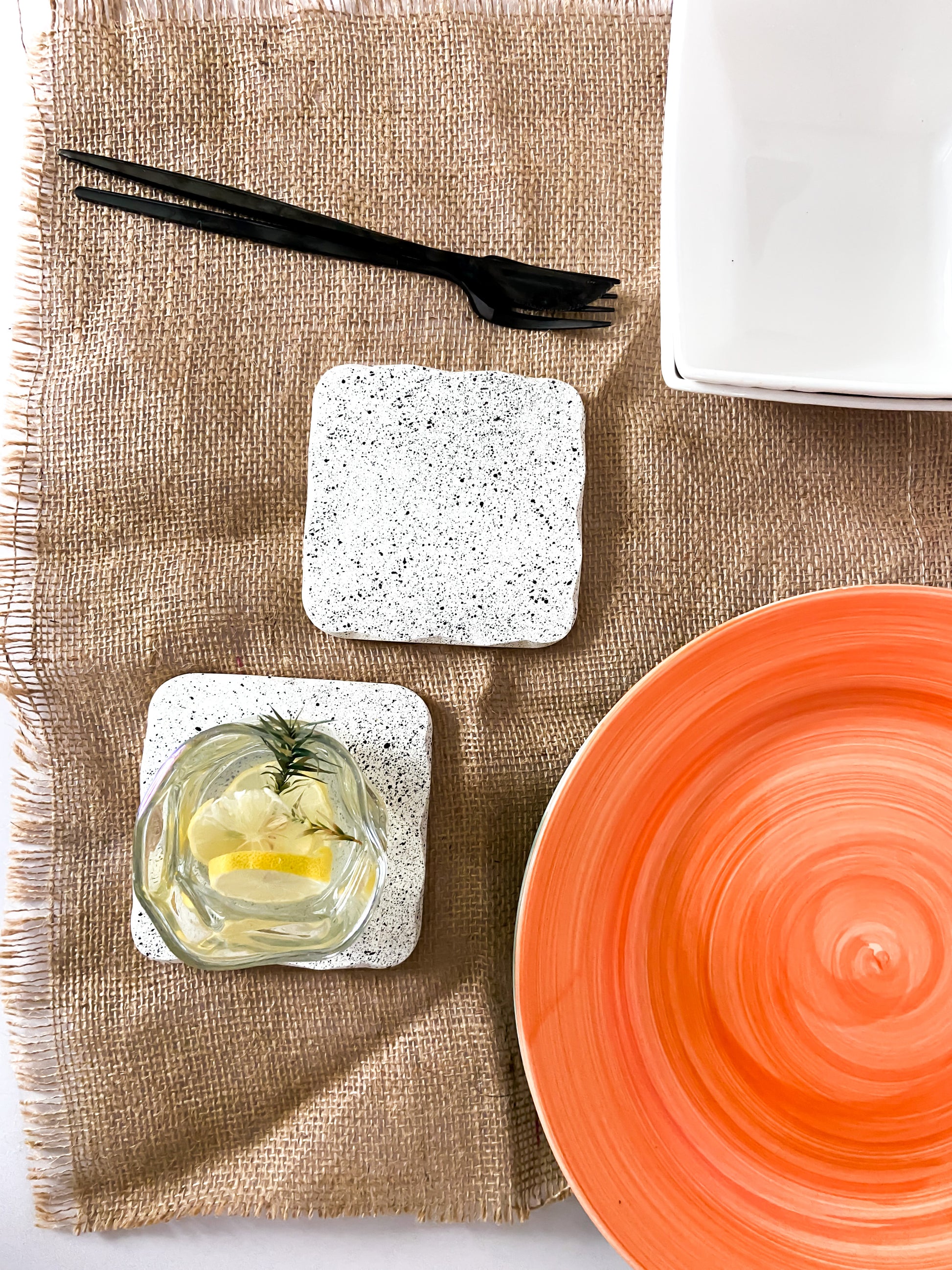 Speckled white concrete coaster set on a burlap table cloth with an orange plate on the right