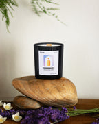 Black candle labeled 'Homebody' on a wooden surface with lavender and flowers in the background