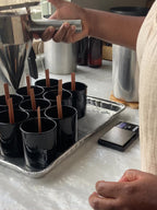 A woman pouring wax into multiple black candle jar on a table.